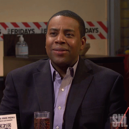 A Man In A Suit Sits In Front Of A Sign That Says Fridays On It GIF