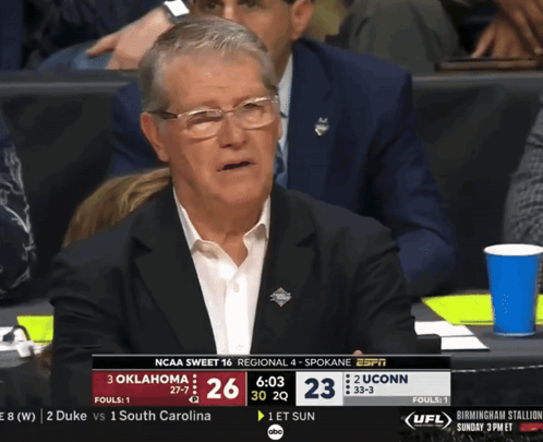 A Man In A Suit Sits In The Stands Watching A Ncaa Basketball Game Between Oklahoma And Uconn GIF
