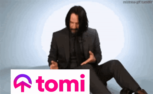 a man in a suit sits next to a sign that says tomi