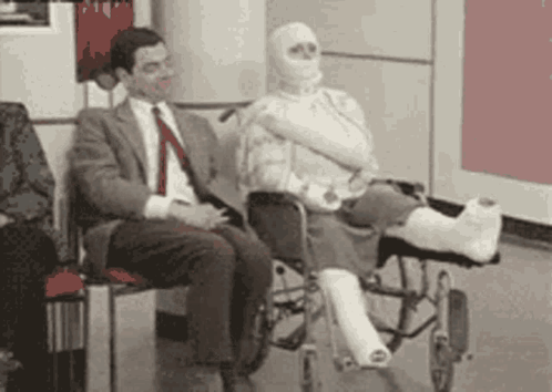 a man in a suit sits next to a woman in a wheelchair with a cast on her leg .