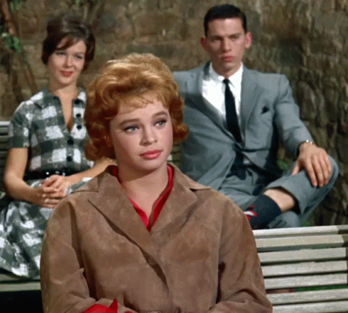 A Man In A Suit Sits On A Bench With Two Women Sitting Behind Him GIF