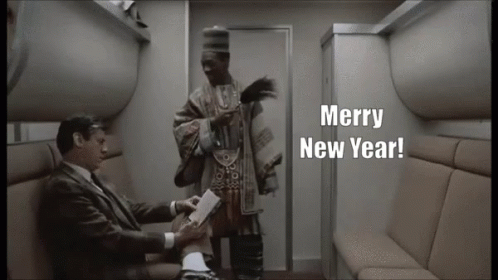 A Man In A Suit Sitting Next To Another Man With Merry New Year Written On The Screen GIF