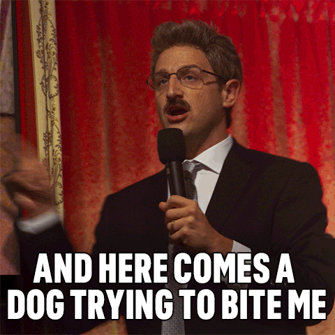 A Man In A Suit Speaking Into A Microphone With The Words And Here Comes A Dog Trying To Bite Me Below Him GIF