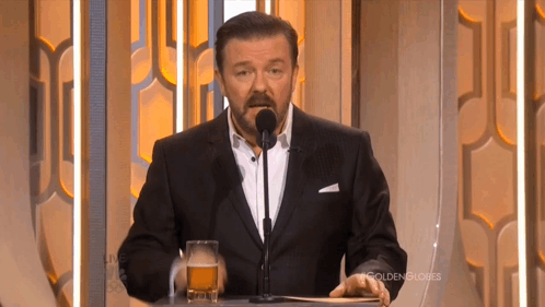 A Man In A Suit Stands At A Podium With A Glass Of Beer In Front Of Him GIF