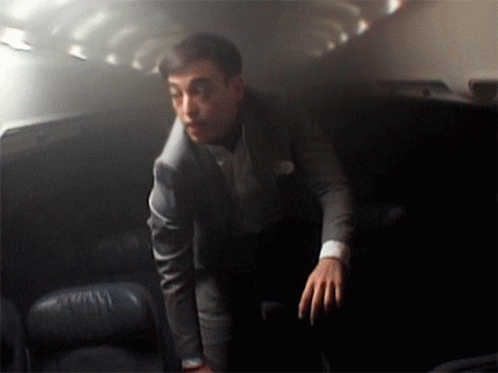 A Man In A Suit Stands In A Dark Room With His Hands On His Hips GIF