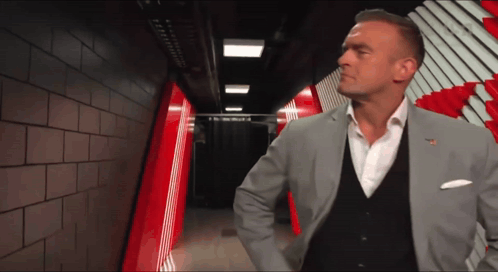 A Man In A Suit Stands In A Hallway With A Red And White Striped Wall Behind Him GIF