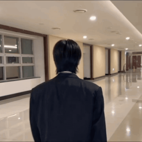 A Man In A Suit Stands In A Hallway With His Back To The Camera GIF