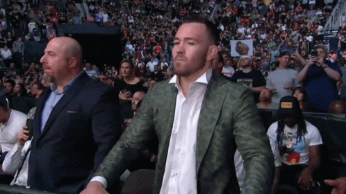 A Man In A Suit Stands In Front Of A Crowd GIF