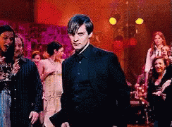 A Man In A Suit Stands In Front Of A Crowd Of People GIF