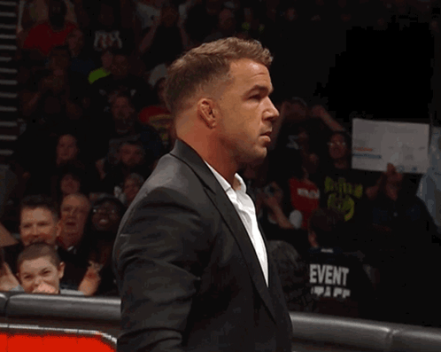A Man In A Suit Stands In Front Of A Crowd With A Sign That Says Tna On It GIF