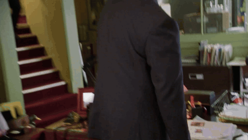 A Man In A Suit Stands In Front Of A Desk With Papers On It GIF