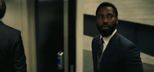 A Man In A Suit Stands In Front Of A Door GIF