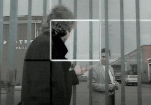 A Man In A Suit Stands In Front Of A Fence With A Sign That Says Porter Prox GIF
