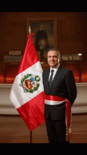 A Man In A Suit Stands In Front Of A Flag GIF