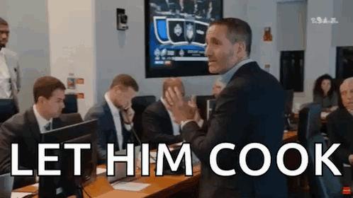A Man In A Suit Stands In Front Of A Group Of People And Says Let Him Cook .. GIF