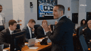 A Man In A Suit Stands In Front Of A Group Of People In Front Of A Screen That Says Tnt GIF