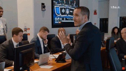 A Man In A Suit Stands In Front Of A Group Of People In Front Of A Screen That Says ' Tsn ' GIF