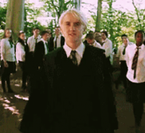 A Man In A Suit Stands In Front Of A Group Of People GIF