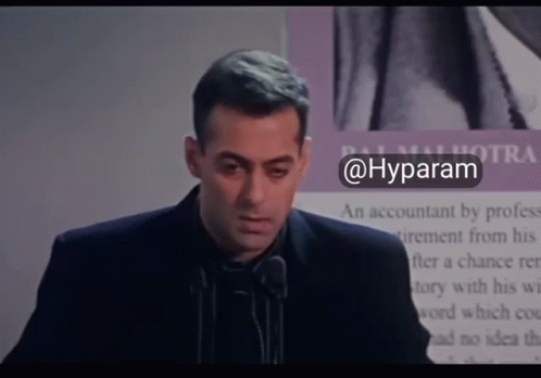 A Man In A Suit Stands In Front Of A Microphone With The Hashtag @Hyparam GIF