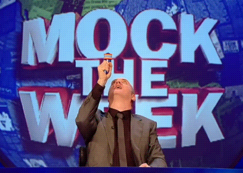 A Man In A Suit Stands In Front Of A Mock The Week Sign GIF
