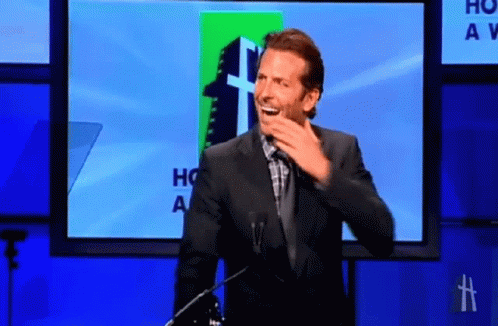A Man In A Suit Stands In Front Of A Screen That Says Ho A V GIF