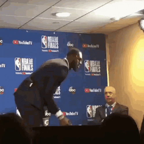 a man in a suit stands in front of a wall with nba finals written on it