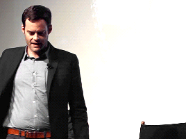 A Man In A Suit Stands In Front Of A White Wall GIF