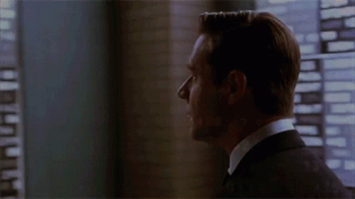 A Man In A Suit Stands In Front Of A Window Looking Out GIF