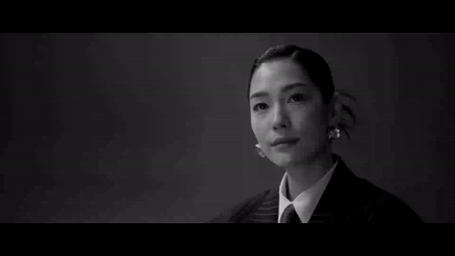A Man In A Suit Stands In Front Of A Woman Sitting At A Table GIF