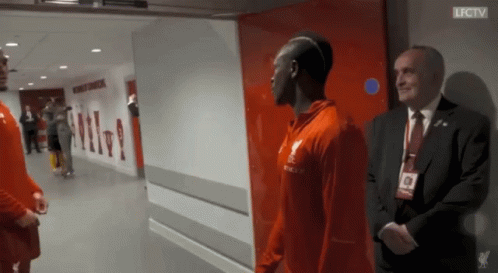 A Man In A Suit Stands Next To A Man In A Red Shirt That Says Lfc Tv GIF