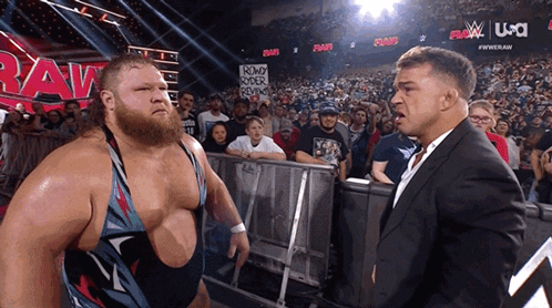 A Man In A Suit Stands Next To A Man In A Wrestling Ring With A Sign That Says Round Rock Reviews GIF