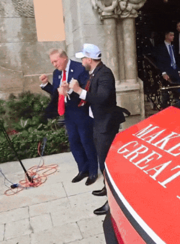 A Man In A Suit Stands Next To A Red Car That Says Make Great GIF