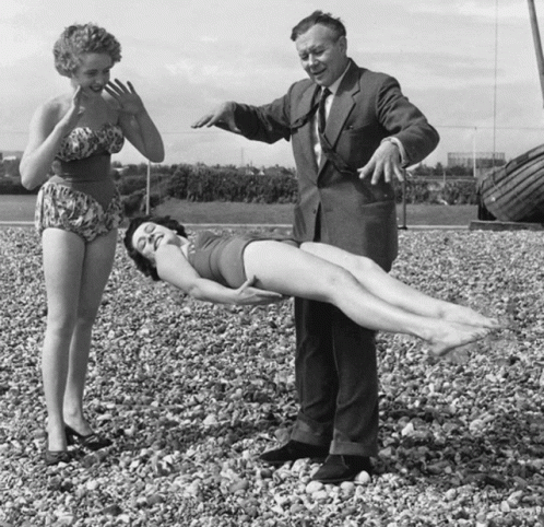 A Man In A Suit Stands Next To A Woman In A Bikini GIF