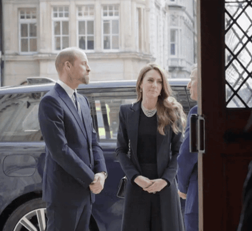 A Man In A Suit Stands Next To A Woman In A Black Dress GIF