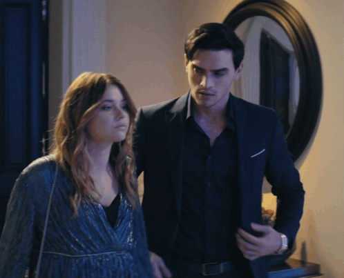 A Man In A Suit Stands Next To A Woman In A Blue Dress GIF