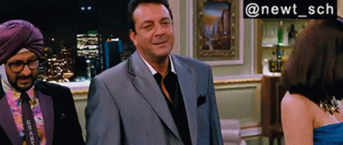A Man In A Suit Stands Next To A Woman In A Blue Dress And A Man In A Turban GIF