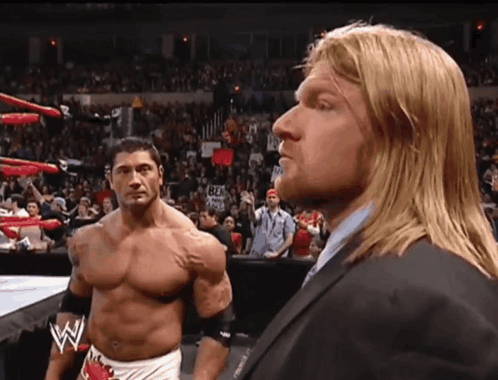 A Man In A Suit Stands Next To Another Man In A Wrestling Ring GIF