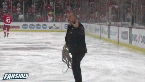 A Man In A Suit Stands On A Hockey Rink In Front Of An Nhl.com Sign GIF