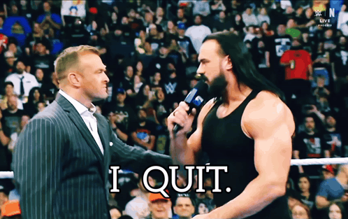 A Man In A Suit Talks Into A Microphone While Another Man Says " I Quit " In Front Of A Crowd GIF