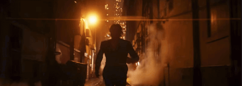 A Man In A Suit Walks Down A Dark Alley At Night GIF