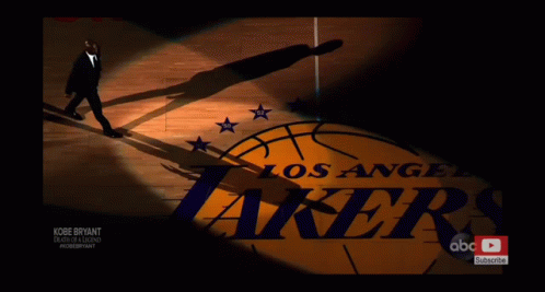 a man in a suit walks on a basketball court with the los angeles lakers logo in the background