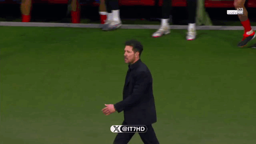 A Man In A Suit Walks On A Soccer Field With A X @ It7hd Logo On The Bottom GIF