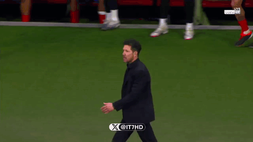A Man In A Suit Walks On A Soccer Field With A X @ It7hd Logo On The Bottom Right GIF