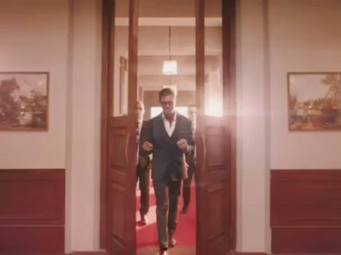 A Man In A Suit Walks Through A Doorway GIF