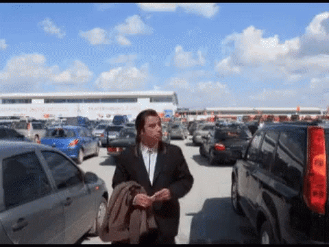 A Man In A Suit Walks Through A Parking Lot GIF