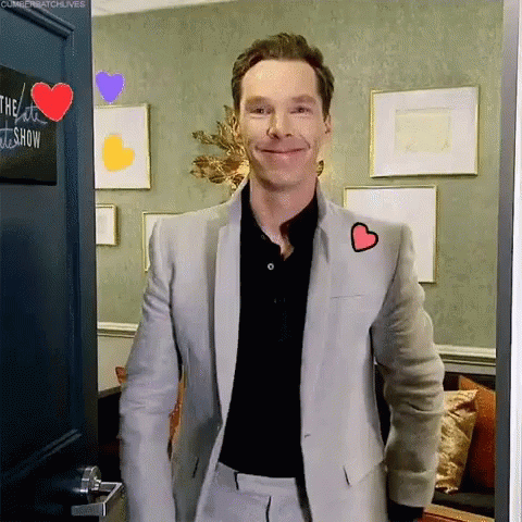 A Man In A Suit With A Heart On His Jacket Is Standing In A Doorway . GIF