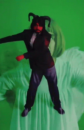 A Man In A Suit With Horns Is Dancing On A Green Background GIF