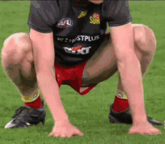 A Man In A Sun Shirt Squatting Down On The Grass GIF