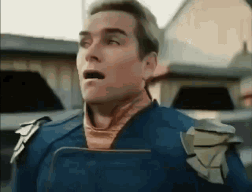 A Man In A Superhero Costume Is Holding A Book In His Hand And Making A Surprised Face . GIF