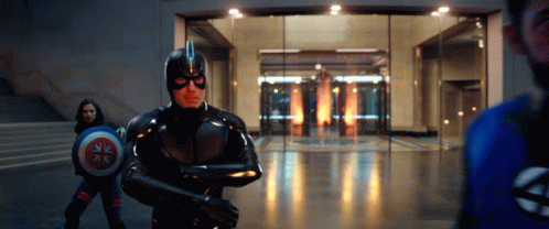 A Man In A Superhero Costume Is Holding A Shield In Front Of A Glass Door . GIF